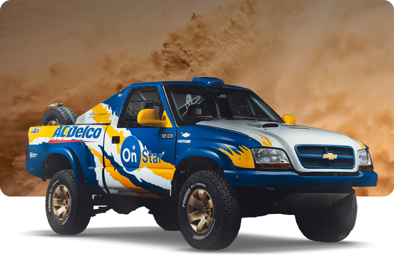 Picape Chevrolet S10 Rally azul e amarela de 2004 em pista de terra, com poeira ao fundo.