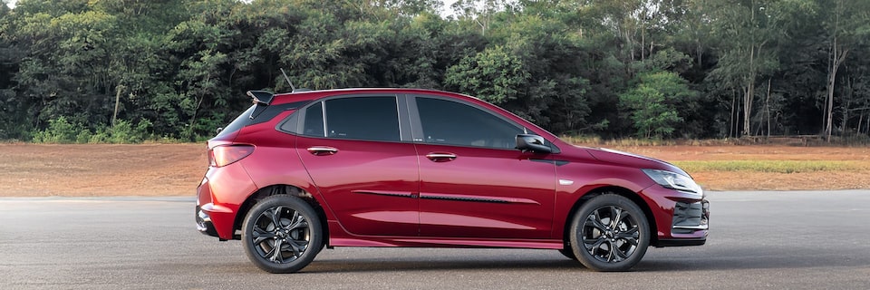 Chevrolet Onix hatch em vista lateral direita com fundo arborizado e sombras suaves no piso.