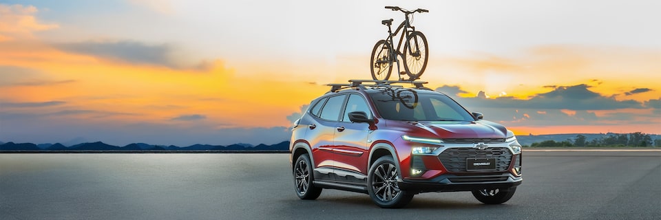 Chevrolet Tracker em vista de frente e lateral direita ao entardecer com bicicleta montada no suporte de teto.