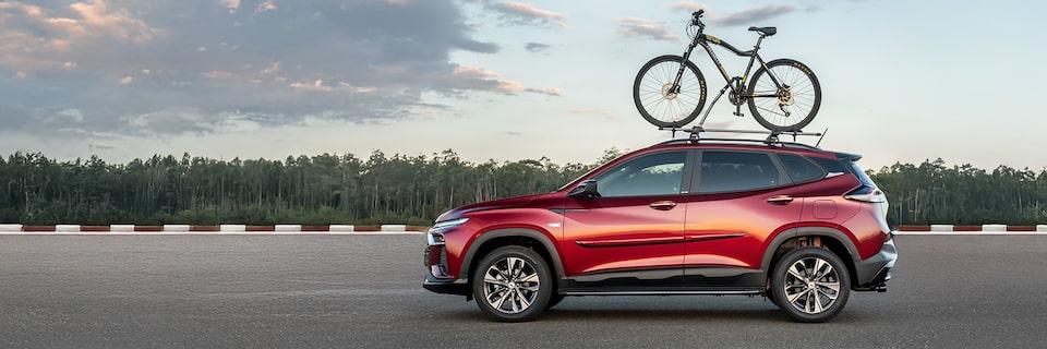 Chevrolet Tracker em vista lateral esquerda com duas bicicletas presas no suporte de teto em cenário aberto.