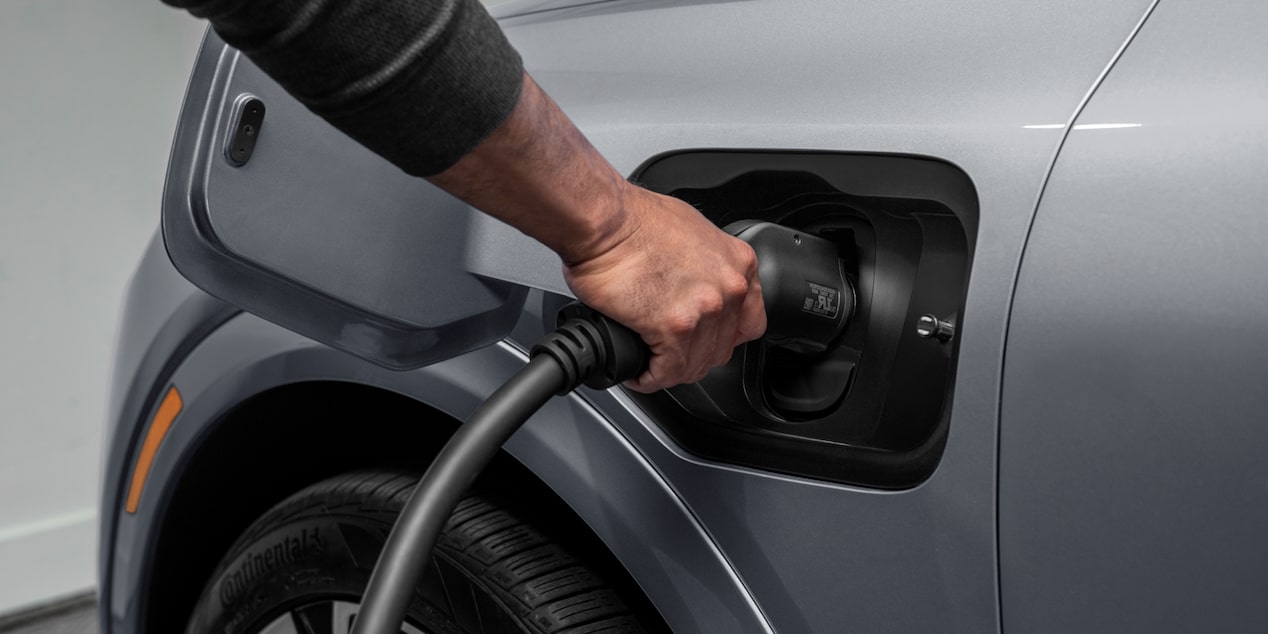 Imagem de um homem plugando o carregador na entrada correspondente de um carro elétrico Chevrolet.