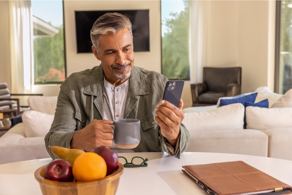 Homem branco com um celular na mão dentro de casa