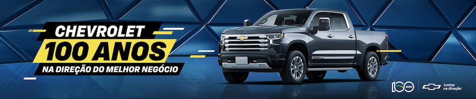 Imagem de uma picape Chevrolet cinza em uma superfície refletiva com um fundo azul geométrico. O texto à esquerda diz Chevrolet 100 Anos, Na Direção do Melhor Negócio. Os logotipos e a marca Chevrolet estão no canto inferior direito.