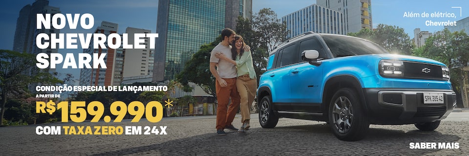 Banner de lançamento do Chevrolet Spark EV visto de frente e lateral direita, estacionado em avenida urbana com prédios altos ao fundo. À esquerda, texto promocional: Novo Chevrolet Spark – condição especial de lançamento a partir de R$ 159.990 com taxa zero em 24x. À frente do carro, um casal sorridente se abraça. No canto superior direito, slogan Além de elétrico, Chevrolet.