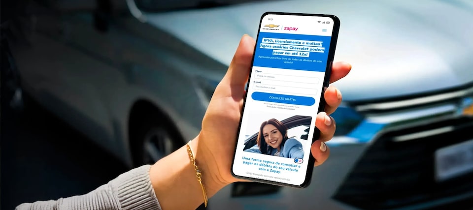 Detalhe de mão feminina segurando um celular cuja tela exibe a solução de pagamento Zapay. No quadrante superior esquerdo, o texto: IPVA 2026 - pague do seu jeito: simples, prático e 100% on-line!
