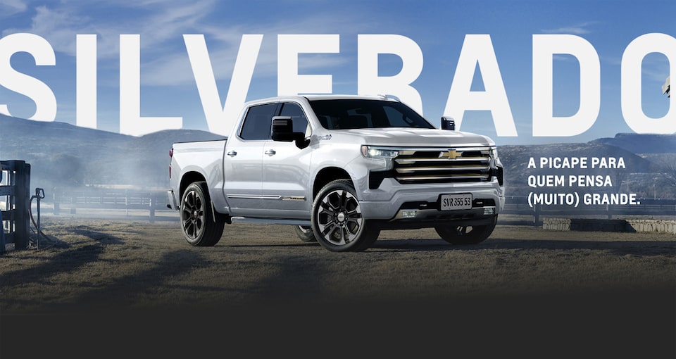 Nova picape Chevrolet Silverado High Country, branco summit, parada em evidência em uma estrada de terra. "Silverado, a picape para quem pensa muito grande".