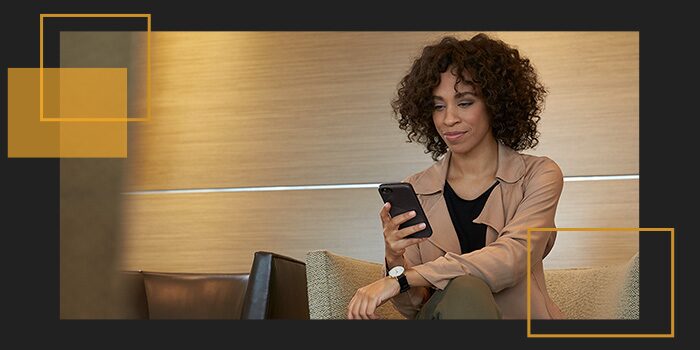 Imagem de mulher preta, executiva, sentada em uma poltrona de escritório, olhando as ofertas Chevrolet, através do "Shop Click Drive", em seu celular.