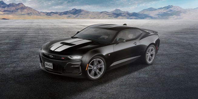 Novo Chevrolet Camaro Colletion coupe, na cor preto, com fachas brancas sobre o capô, sobre asfalto acinzentado.
