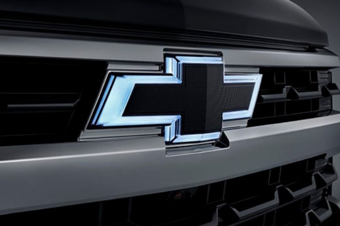 Imagem em close da grade dianteira da nova picape Chevrolet Silverado, preto, dando destaque ao logo Chevrolet "iluminado" com neon em sua volta.