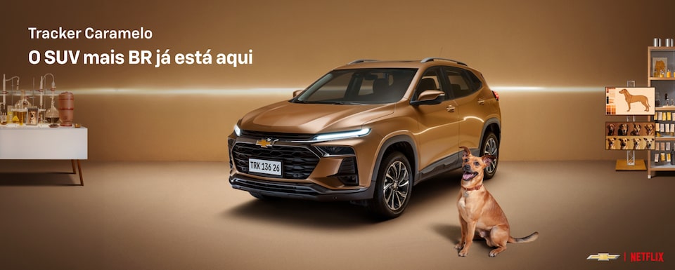 Tracker Caramelo em estúdio com fundo iluminado, acompanhado de um cachorro caramelo sentado à frente. Texto no topo esquerdo diz Tracker Caramelo – O SUV mais BR já está aqui.