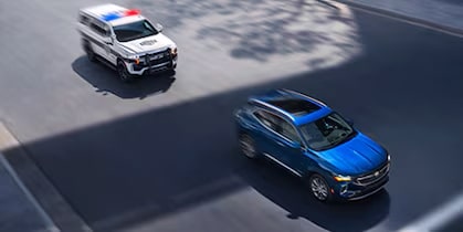 Carro azul andando na rua e um carro de policia atrás perseguindo