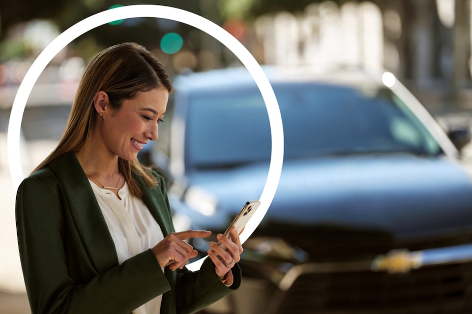 Imagem de uma mulher usando o serviço OnStar em seu celular, parada ao lado de seu Chevrolet.