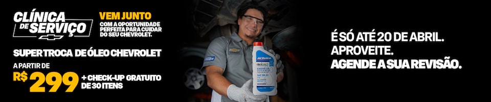 Um mecânico segura uma garrafa de óleo de motor em uma oficina mecânica. O texto promocional oferece troca de óleo Chevrolet a partir de R$ 299 e revisão gratuita de 30 itens até 20 de abril.