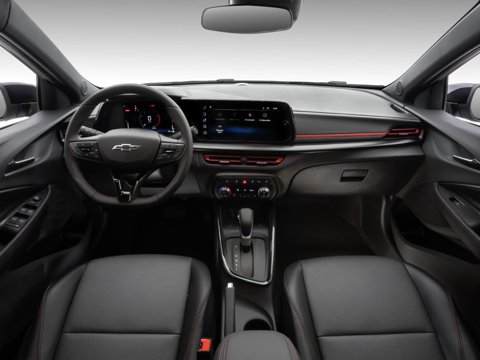 Visão interna do Chevrolet Sonic. Vemos todo o painel do veículo, o volante, painel de instrumentos, Chevrolet MyLink e parte dos bancos do motorista e passageiro.