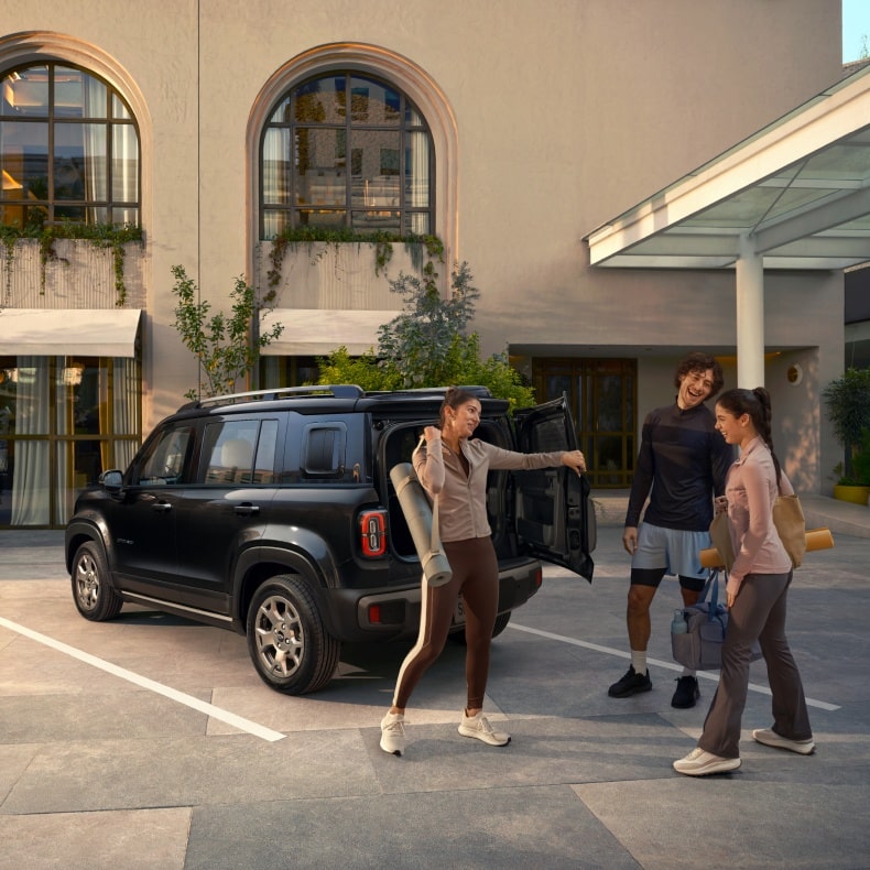 Um Spark EUV preto estacionado em uma vaga. Próximo ao carro, temos duas mulheres e um homem prontos para praticarem esportes.