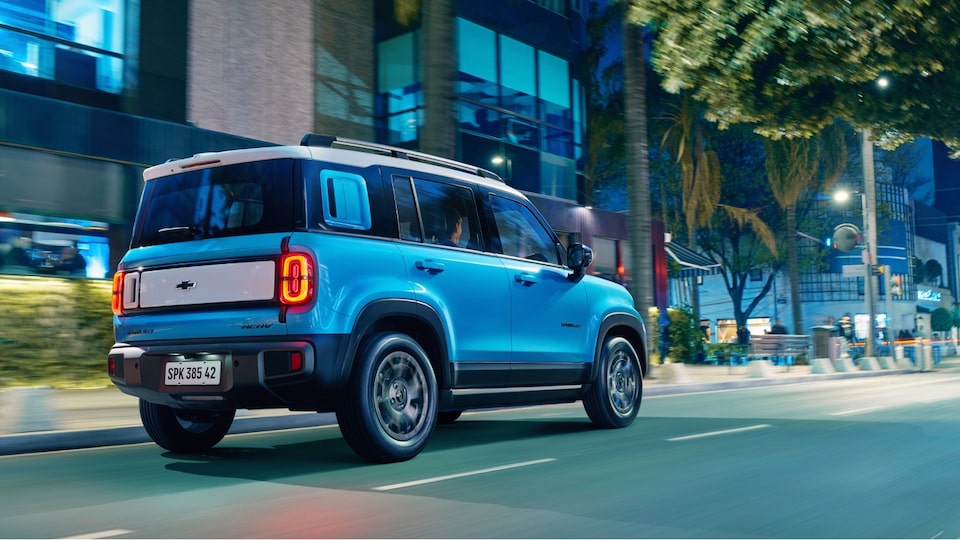 Spark EUV Azul Atlântico andando na rua. Vemos parte da lateral e traseira do veículo. Ao fundo, temos algumas árvores e prédios comerciais.