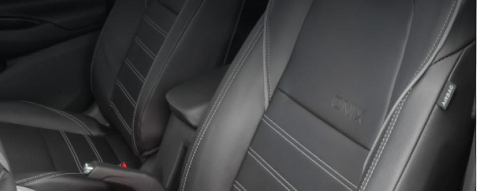 Detalhe dos bancos do motorista e do passageiro que ilustra a página da da linha de acessórios originais Chevrolet para o Chevrolet Onix Plus. No quadrante superior esquerdo, o texto: Onix - Conforto.