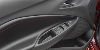 Detalhe da roda do Chevrolet Onix hatch vermelho, com aro escurecido e design esportivo, em destaque sobre asfalto urbano.