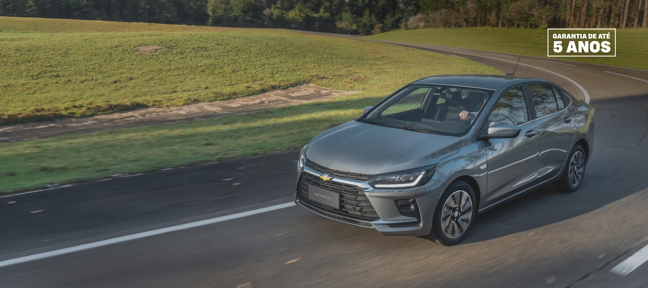 Chevrolet Onix Plus 2027 na cor prata shark em movimento em uma estrada.
