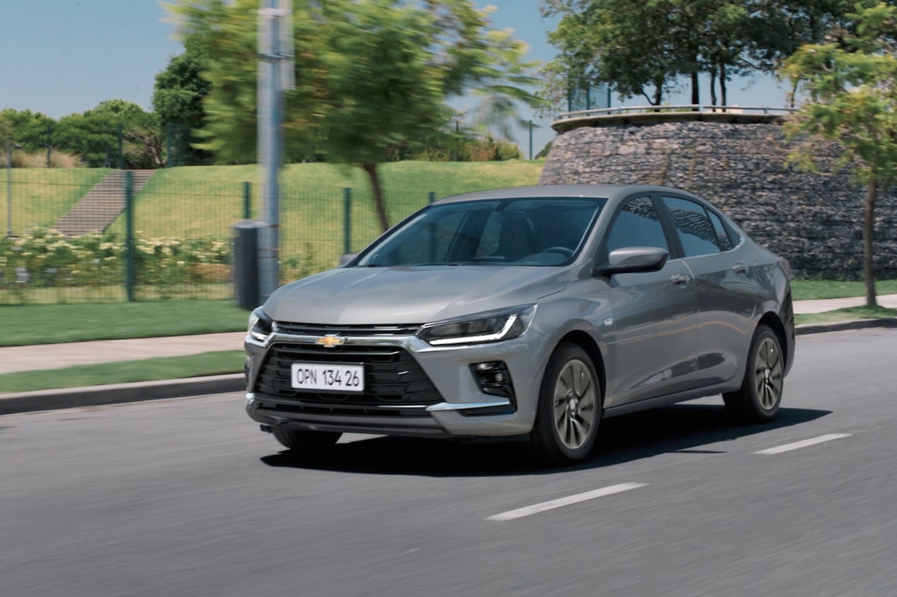 Chevrolet Onix Plus na cor Prata Shark em movimento em rua arborizada.