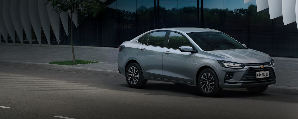 Chevrolet Onix Plus prata estacionado em uma rua de paralelepípedos, com fachada urbana ao fundo.