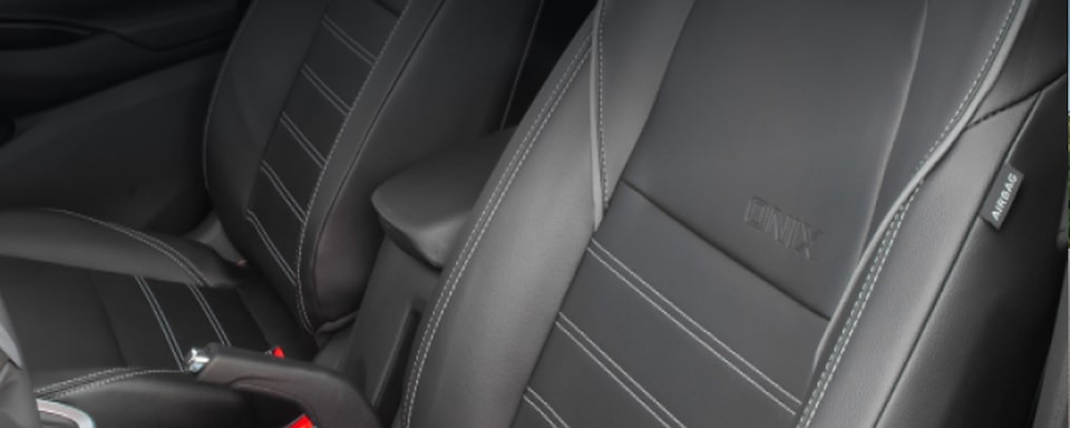 Detalhe dos bancos do motorista e do passageiro que ilustra a página da da linha de acessórios originais Chevrolet para o Chevrolet Onix HB. No quadrante superior esquerdo, o texto: Onix - Conforto