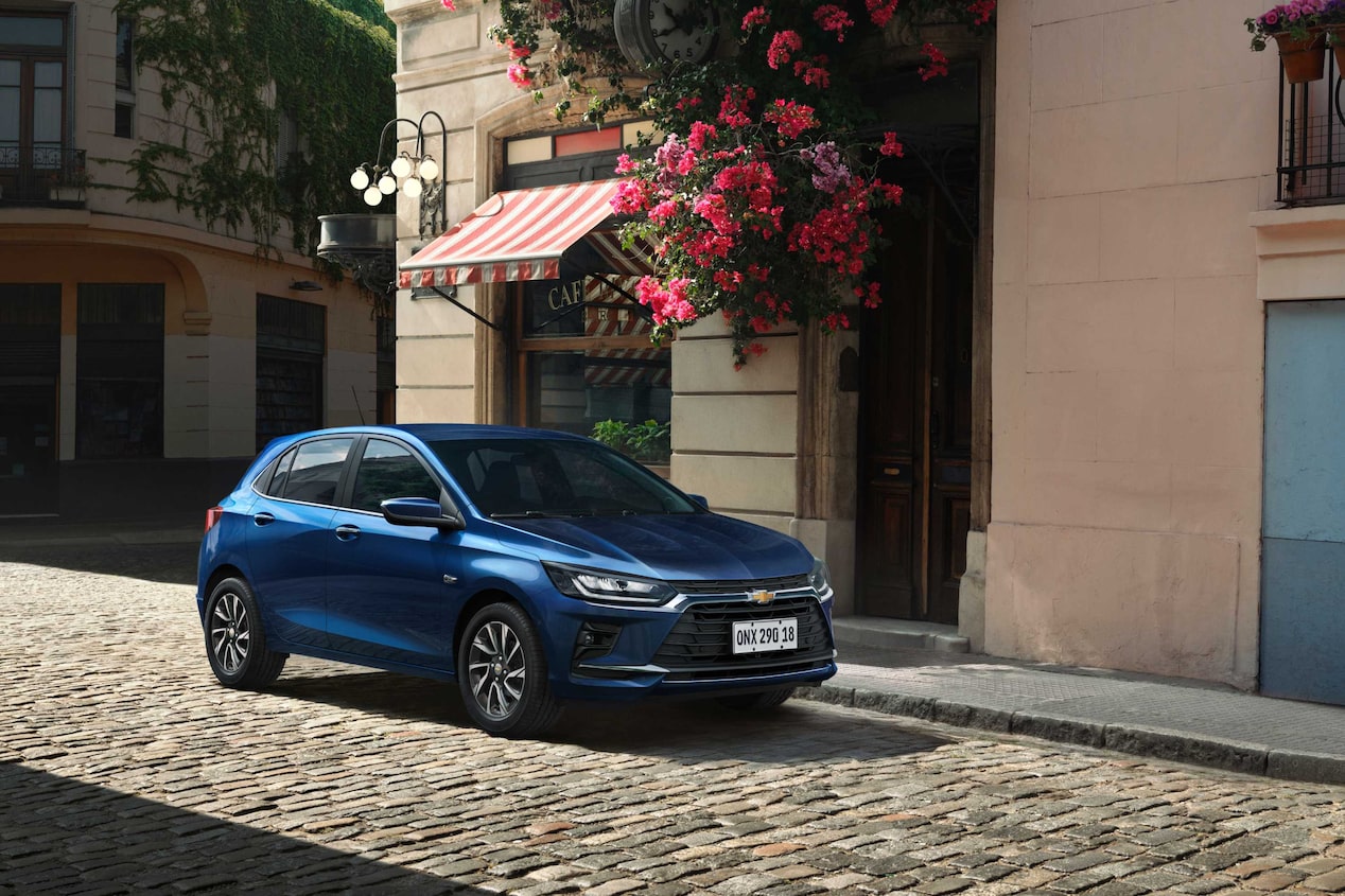 Chevrolet Onix Azul Boreal estacionado em rua de paralelepípedo, com fachada florida ao fundo.