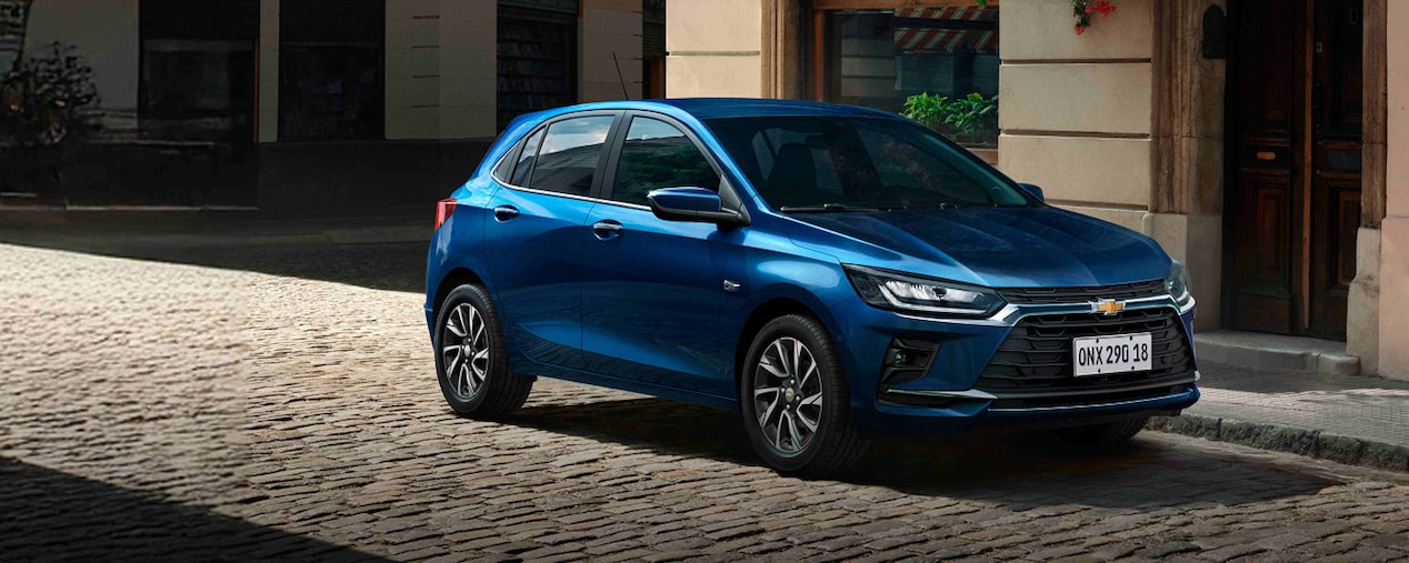 Chevrolet Onix azul estacionado em uma rua de paralelepípedos, com fachada urbana ao fundo.