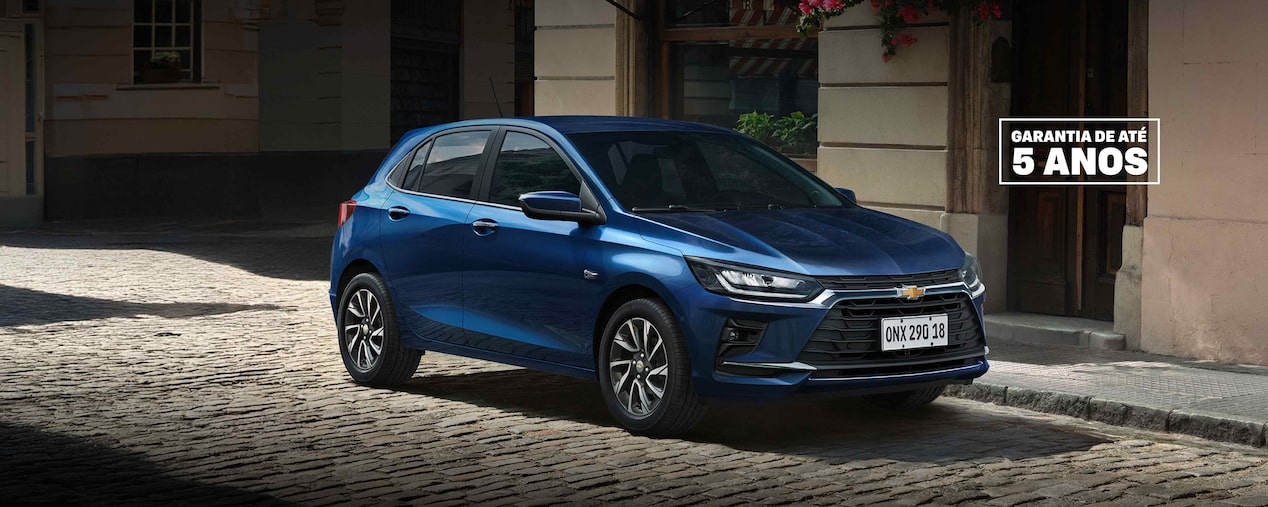 Chevrolet Onix azul estacionado em uma rua de paralelepípedos, com fachada urbana ao fundo.