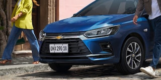 Chevrolet Onix hatch azul em rua de paralelepípedo, destaque para frente do carro com faróis LED e design moderno em cenário urbano.