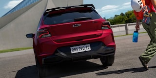 Chevrolet Onix hatch vermelho visto de traseira em rua urbana, com design esportivo, lanternas escurecidas, spoiler e acabamento moderno.