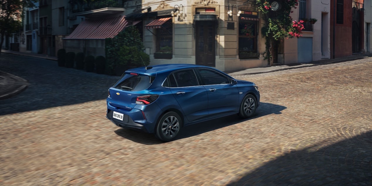 Chevrolet Onix hatch azul em movimento visto de traseira em rua urbana, com design moderno, lanternas em LED e estilo compacto.