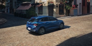 Chevrolet Onix hatch azul em movimento visto de traseira em rua urbana, com design moderno, lanternas em LED e estilo compacto.