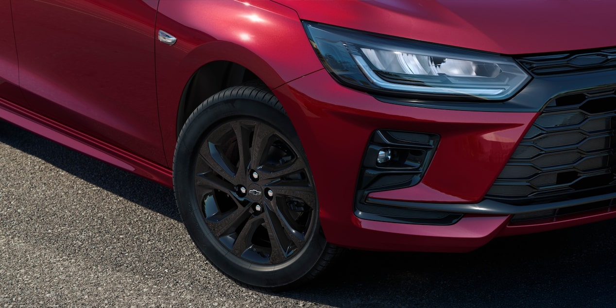 Detalhe da roda do Chevrolet Onix hatch vermelho, com aro escurecido e design esportivo, em destaque sobre asfalto urbano.