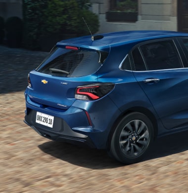 Chevrolet Onix hatch azul em movimento visto de traseira em rua urbana, com design moderno, lanternas em LED e estilo compacto.