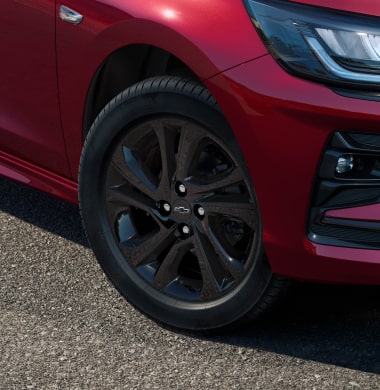 Detalhe da roda do Chevrolet Onix hatch vermelho, com aro escurecido e design esportivo, em destaque sobre asfalto urbano.