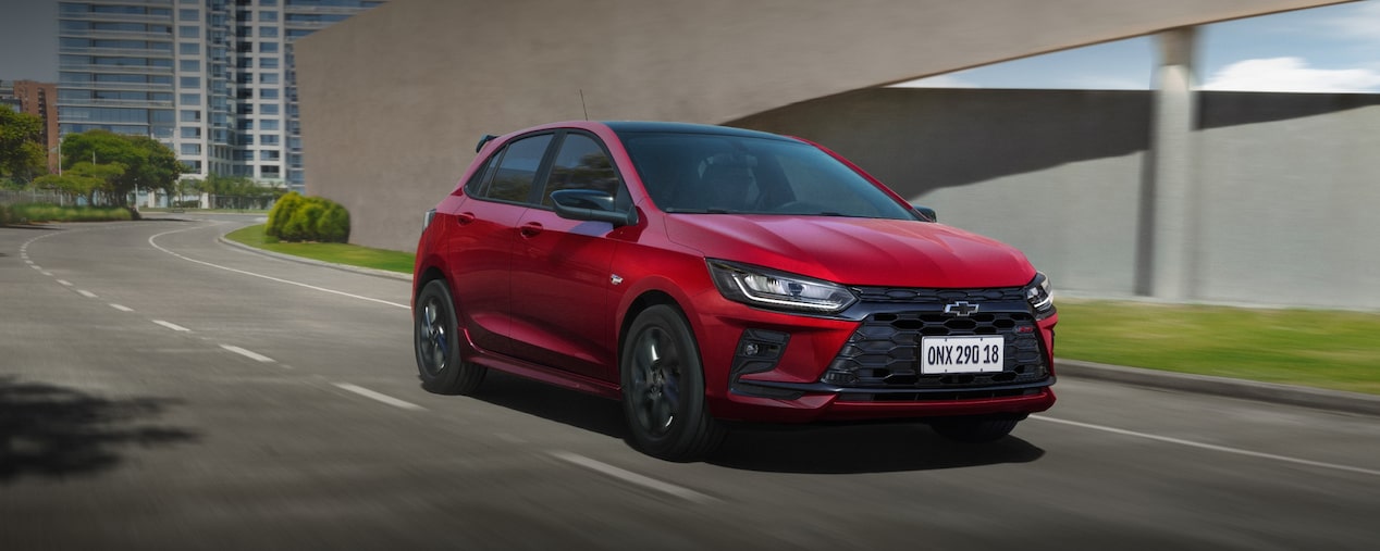 Chevrolet Onix RS 2027 vermelho em movimento na cidade, hatch compacto com design moderno, faróis em LED esportivos.