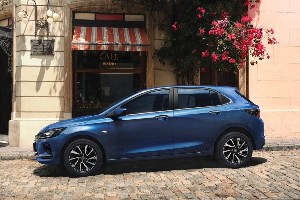 Chevrolet Onix HB azul estacionado em rua de paralelepípedo em frente a café bistrô com fachada clássica e flores decorativas
