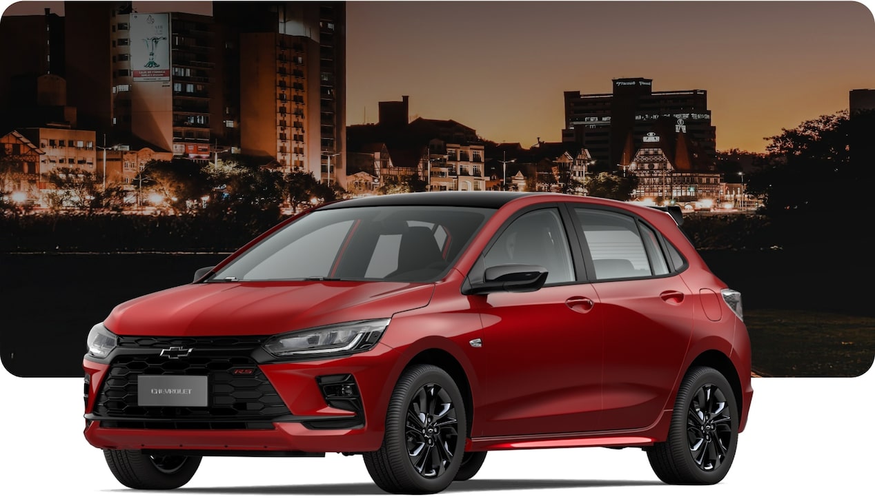 Chevrolet Onix RS Turbo AT hatch vermelho em cidade à noite, com design esportivo, rodas escuras e visual moderno em cenário urbano iluminado.