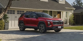 Equinox RS visto de frente e lateral esquerda, estacionado em entrada residencial pavimentada, com garagem e jardim ao fundo sob luz natural.