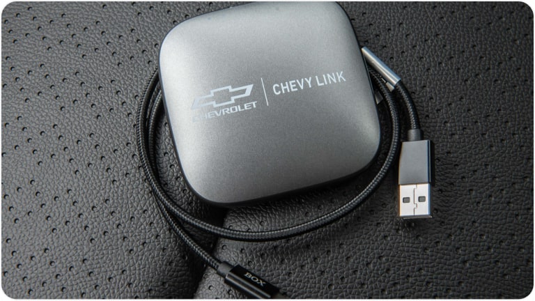 Imagem do device Chevy Link em primeiro plano, apoiado sobre o banco do Chevrolet Tracker 2026