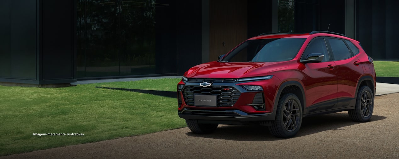 Chevrolet Tracker RS vermelha estacionada em frente a edifício moderno, destacando a grade frontal esportiva, rodas escurecidas e detalhes exclusivos da versão RS.