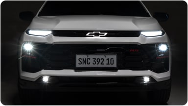 Parte frontal do Chevrolet Sonic. O ambiente ao redor está todo escuro e as lanternas e faróis estão acesas.