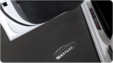 A porta do Chevrolet Sonic aberta e o logo Sonic iluminado no chão.