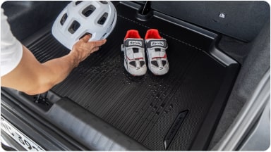 Parte interna do veículo com foco no tapete do porta-malas. Dentro do porta-malas tem um capacete e um par de sapatilhas de ciclismo e alguém está pegando o capacete.