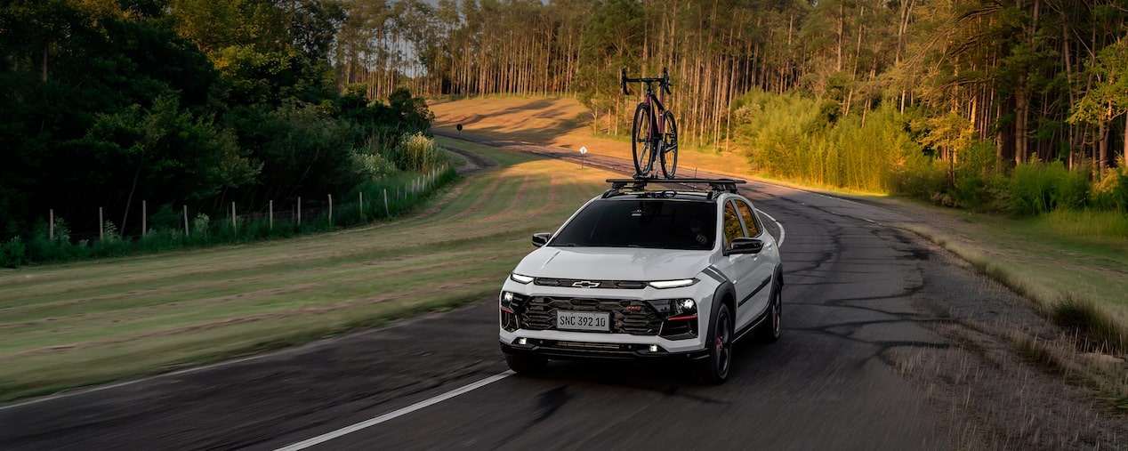 Chevrolet Sonic em movimento em uma estrada. Ao fundo vemos alguns arbustos e árvores. Em cima do veículo há uma bicicleta fixada no rack de teto. No canto superior esquerdo, o texto: Sonic. Entretenimento