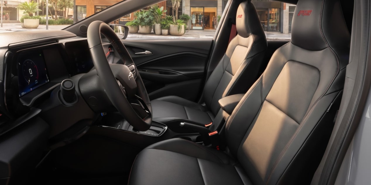 Visão em primeira pessoa do interior do carro. Temos em quadro o volante e o banco do motorista e passageiro.