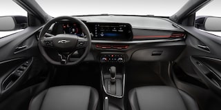 Visão em primeira pessoa do motorista. Temos o volante com o logo da Chevrolet no centro, o painel de instrumentos  e a central multimídia, câmbio automático e parte dos bancos.​