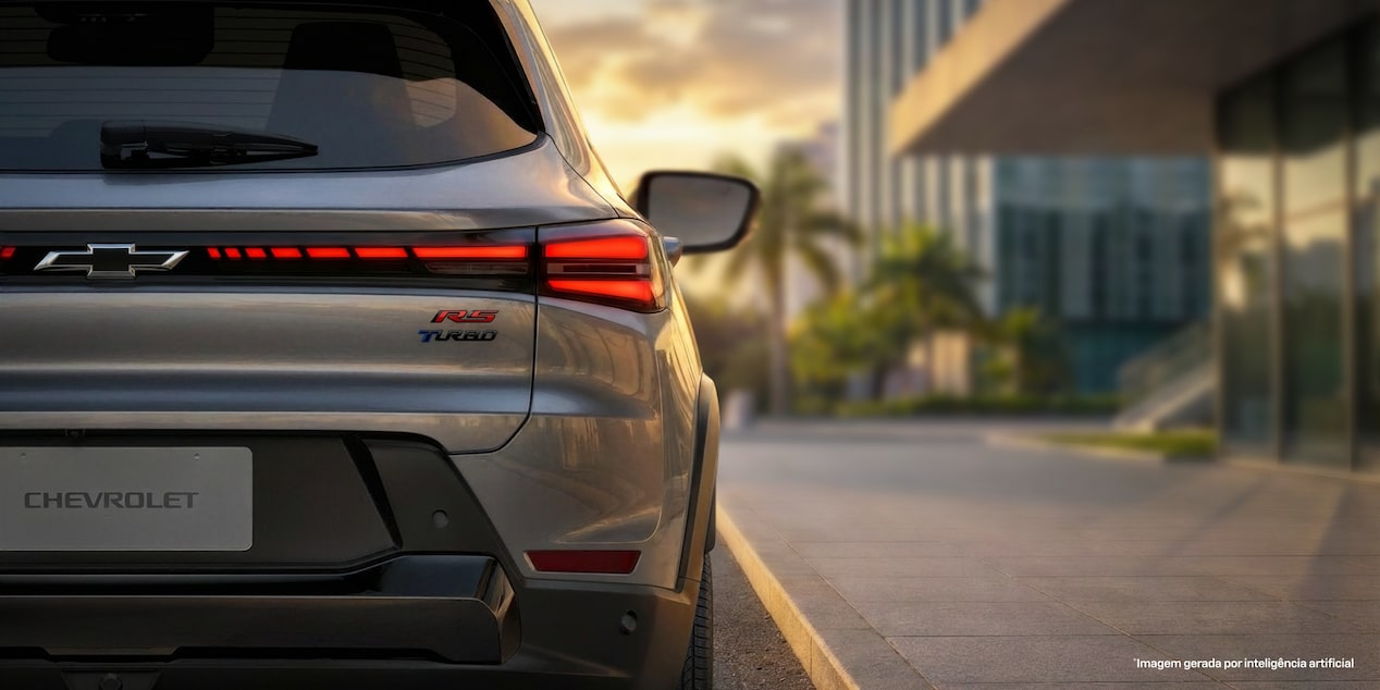 O Chevrolet Sonic está estacionado na rua. Ao fundo, o céu de fim de tarde dá um tom amarelado para a imagem. Foco na traseira do Chevrolet Sonic e destaque as as luzes em LED vermelho e o nome do veículo. ​