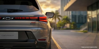 O Chevrolet Sonic está estacionado na rua. Ao fundo, o céu de fim de tarde dá um tom amarelado para a imagem. Foco na traseira do Chevrolet Sonic e destaque as as luzes em LED vermelho e o nome do veículo. ​